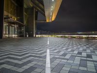 a wide open square has a black paved area and buildings at night in the background