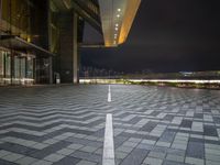 a wide open square has a black paved area and buildings at night in the background