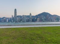 a man walks across the grass towards the water in the city park area of an urban area