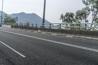 an empty road on the side of a mountain with trees in the background and mountains in the distance