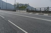 an empty road on the side of a mountain with trees in the background and mountains in the distance