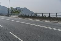 an empty road on the side of a mountain with trees in the background and mountains in the distance