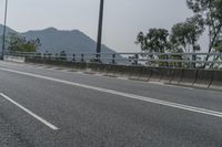 an empty road on the side of a mountain with trees in the background and mountains in the distance