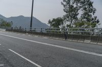 an empty road on the side of a mountain with trees in the background and mountains in the distance