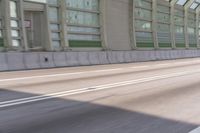 the motorcycle is white in color riding on the road near a glass wall and a building