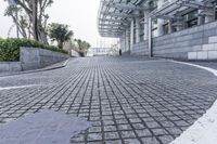 a paved driveway is surrounded by large concrete walling and trees that overlook to a modern building