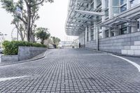 a paved driveway is surrounded by large concrete walling and trees that overlook to a modern building