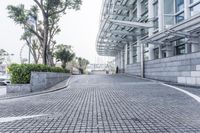 a paved driveway is surrounded by large concrete walling and trees that overlook to a modern building