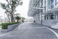 a paved driveway is surrounded by large concrete walling and trees that overlook to a modern building