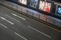 the car is waiting for the subway to pass by at night time and a sign on the side of the street has an arrow pointing upwards at left