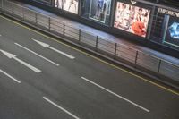the car is waiting for the subway to pass by at night time and a sign on the side of the street has an arrow pointing upwards at left