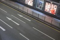 the car is waiting for the subway to pass by at night time and a sign on the side of the street has an arrow pointing upwards at left