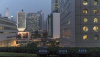 several bins on top of a grassy area by some tall buildings with windows on the side