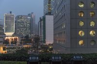 several bins on top of a grassy area by some tall buildings with windows on the side