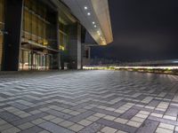 the sidewalk and walkway outside an office building at night near a dock with lights on