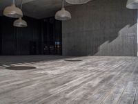 wooden flooring inside of a big building under multiple lamps hanging from a ceiling over it