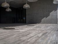 wooden flooring inside of a big building under multiple lamps hanging from a ceiling over it