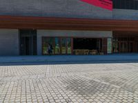 a brick walkway in front of an auditorium building with people standing at the doors in front