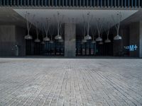 a building with various lamps in front of it on a brick floor and stone pillars