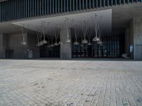 a woman walking past an empty building next to tall buildings and metal lighting fixtures hanging from the ceiling