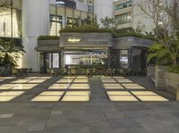 an urban plaza with tables and plants on one floor and people sitting and standing in the center