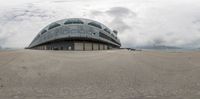 a curved building on an empty, windy day with clouds behind it in the foreground