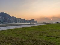 a park and a beach near the water at sunset with skyscrapers in the background