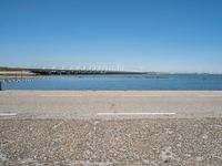 a view from the side of a concrete area near some water and the sky in the background