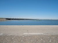 a view from the side of a concrete area near some water and the sky in the background