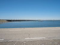 a view from the side of a concrete area near some water and the sky in the background