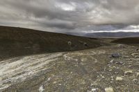 horse running in a dry landscape under cloudy skies and black clouds by itself, with grey rocks strewn all around