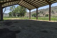 a horse under a shelter at an outdoor area with grass and mountains in the distance