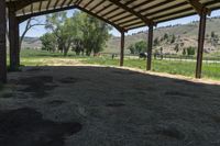 a horse under a shelter at an outdoor area with grass and mountains in the distance