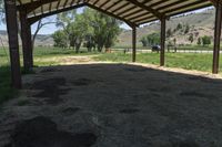 a horse under a shelter at an outdoor area with grass and mountains in the distance