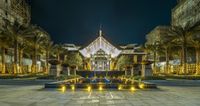 the hotel courtyard has fountains lit up at night with greenery in foreground and large windows