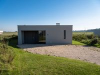 an empty concrete house sits alone in a field and has a parking space on the side of it