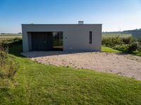 an empty concrete house sits alone in a field and has a parking space on the side of it