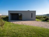 an empty concrete house sits alone in a field and has a parking space on the side of it