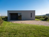 an empty concrete house sits alone in a field and has a parking space on the side of it