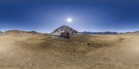 a small house sits in the middle of a desert area in front of mountains with snow