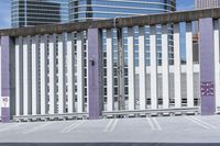 a tall metal fence on top of a cement floor under a building tower with graffiti written on it