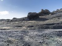 a barren landscape with rocks and bushes near by a road in the desert under a blue sky