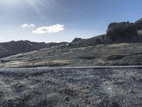 a barren landscape with rocks and bushes near by a road in the desert under a blue sky