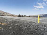 a yellow sign is sitting on a rocky beach and mountains are in the background a body of water is visible