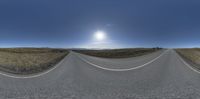 360 - view of a road going through the sun and hills, with a bright blue sky and mountains in the background