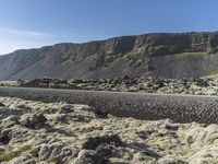 a winding road between boulders and mountains on a sunny day in iceland is shown as a lone car drives by