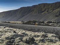 a winding road between boulders and mountains on a sunny day in iceland is shown as a lone car drives by