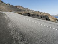 an empty road going into the distance between hills and a body of water with a person on it