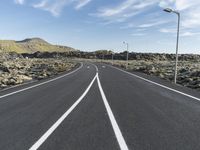 a highway that has white lines and gravel with a hill in the background with some street lights in the distance