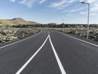 a highway that has white lines and gravel with a hill in the background with some street lights in the distance